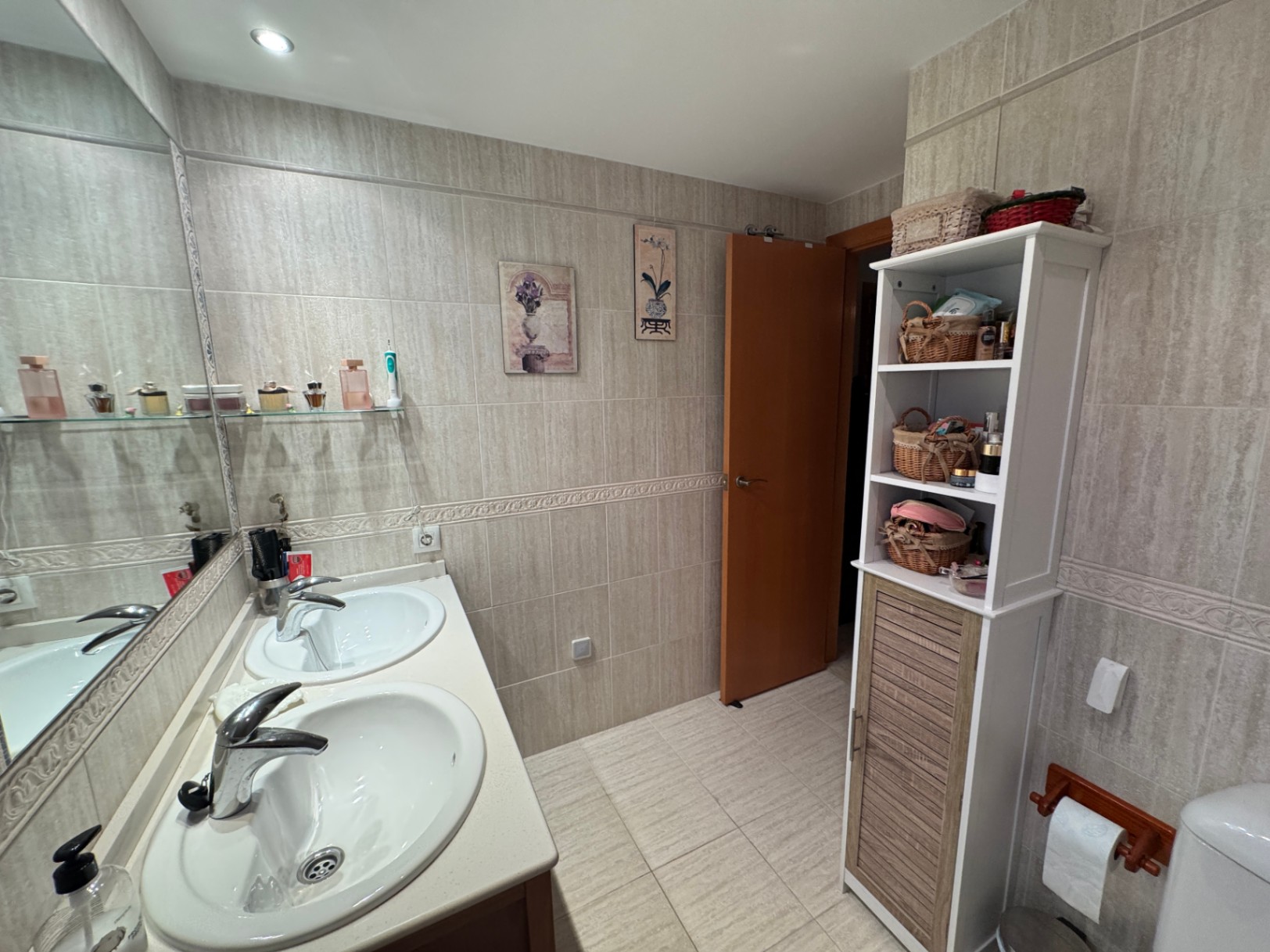 Salle de bain avec meuble-lavabo double vasque, miroir et étagère de rangement.