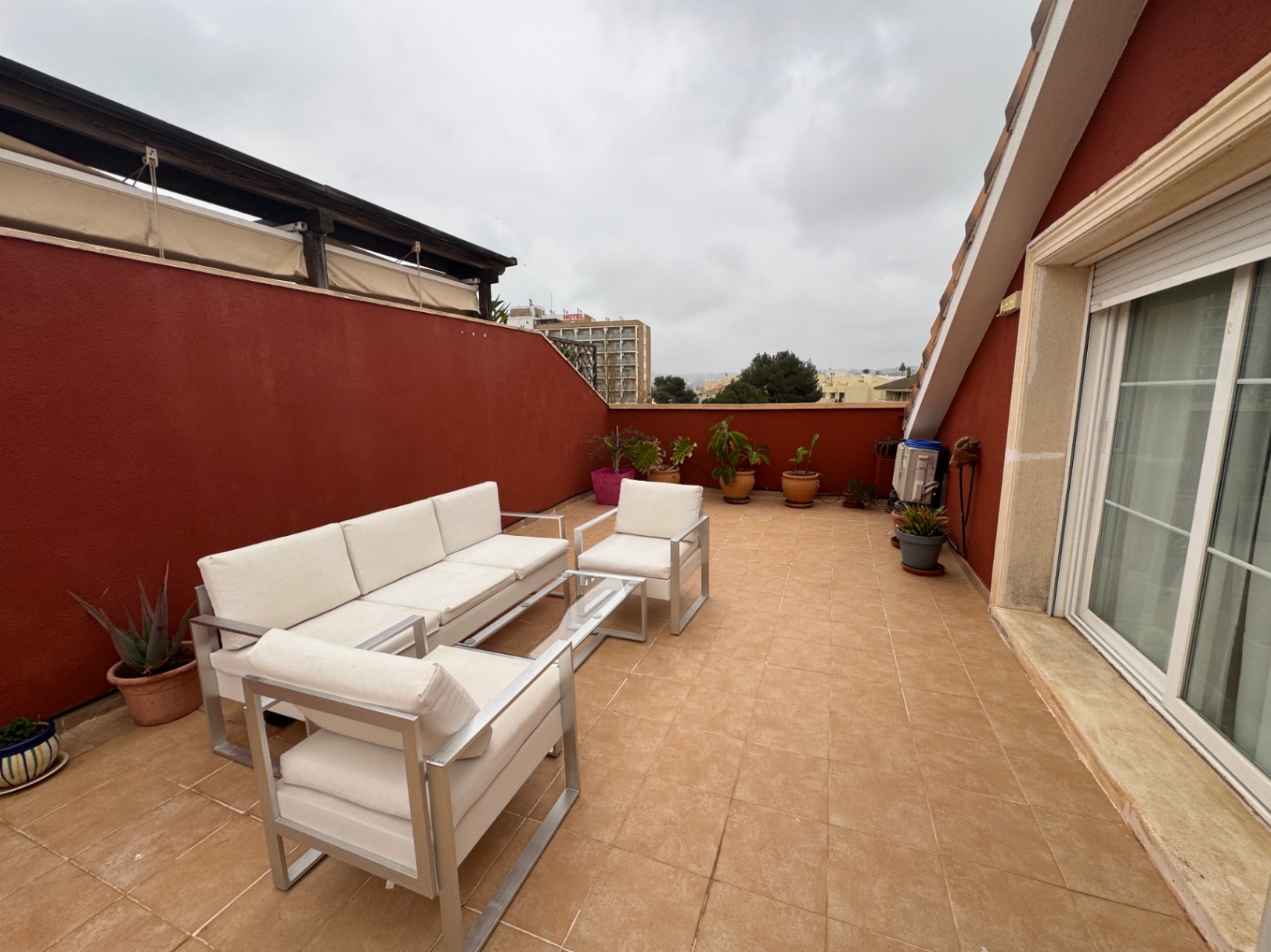 Terrasse avec sol en céramique, murs rouges et mobilier d'extérieur en aluminium.