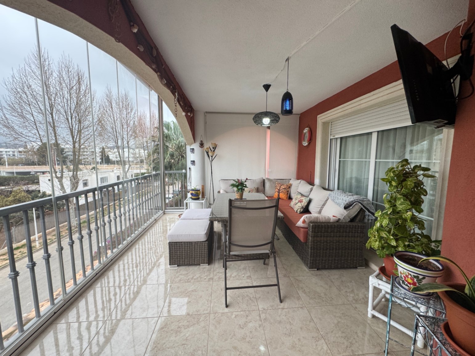 Terrasse couverte avec fermeture en verre, sol carrelé et vue urbaine.