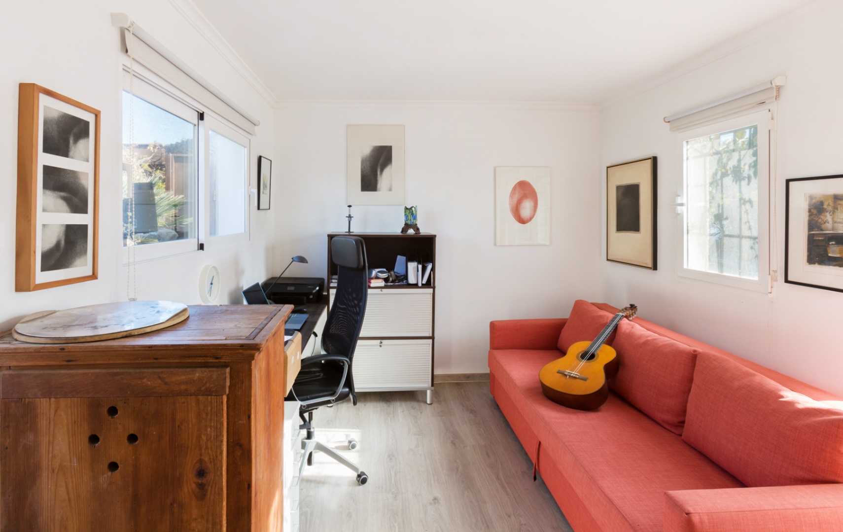 Bureau à domicile lumineux avec parquet clair, comprenant un canapé rouge, un espace de travail ergonomique et une lumière naturelle traversante.