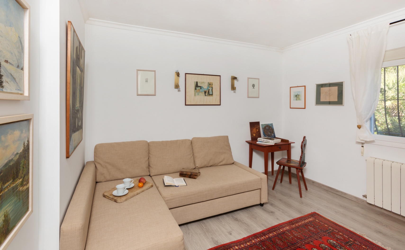 Coin salon lumineux avec canapé méridienne beige, bureau en bois classique et galerie d'art murale sur un sol stratifié gris clair.