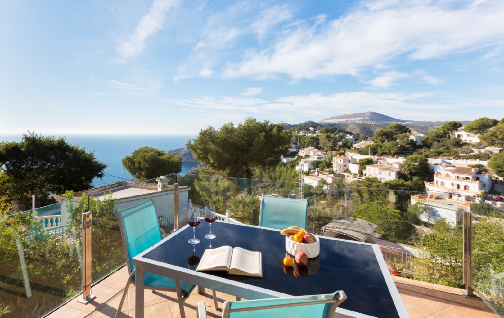 Terrasse avec garde-corps en verre, table à manger en verre noir et vue panoramique sur la côte méditerranéenne et les collines de Cumbre del Sol.