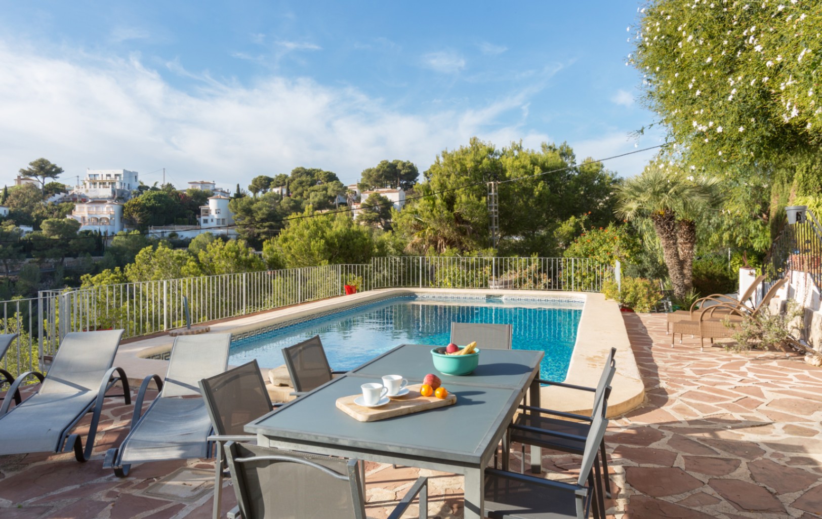 Terrasse extérieure en dalles de pierre naturelle avec piscine rectangulaire, coin repas et transats, bordée par une végétation méditerranéenne dense.