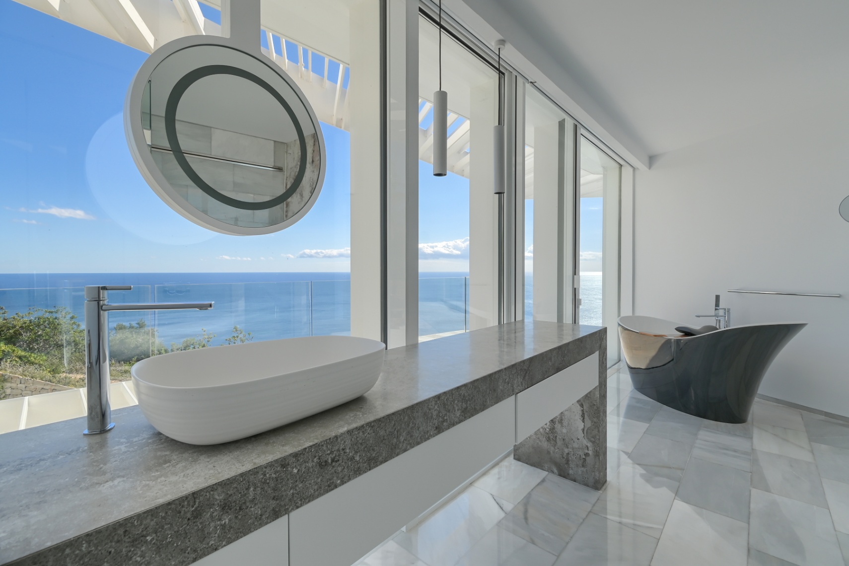Salle de bain moderne avec plan de toilette en pierre grise, vasque à poser et baignoire îlot design, offrant des vues panoramiques sur la mer.