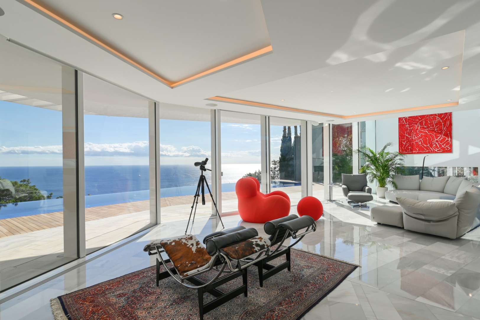 Salon lumineux doté de baies vitrées, d'un sol en marbre et de mobilier design offrant une vue panoramique sur la piscine à débordement et la mer.