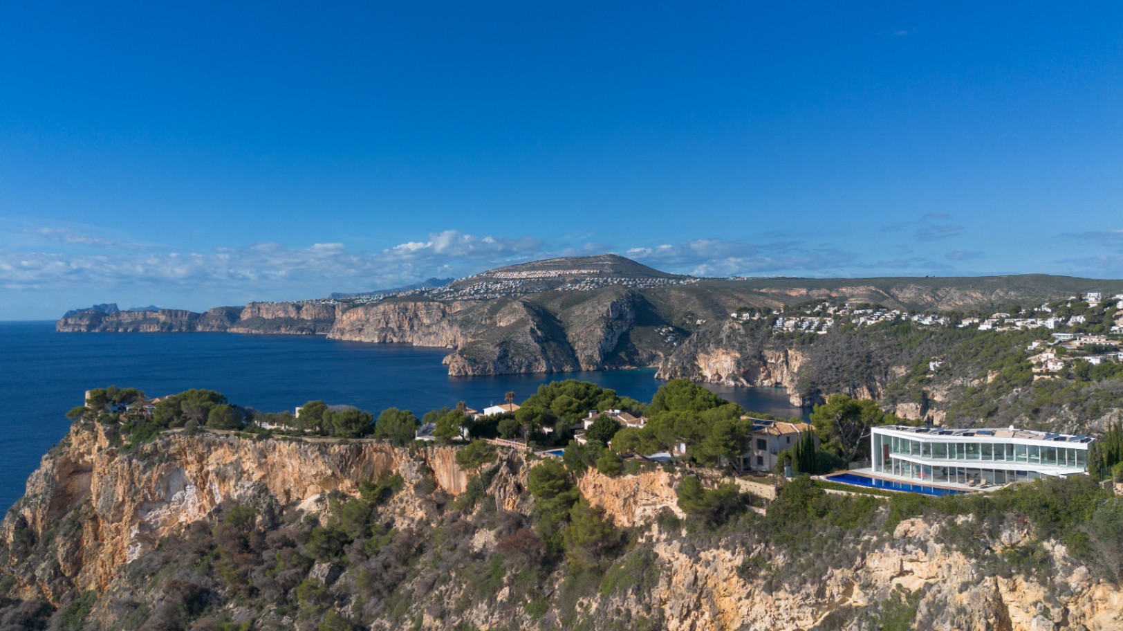 Vue aérienne d'une villa contemporaine vitrée sur une falaise, avec une piscine linéaire et une vue panoramique sur le littoral méditerranéen.