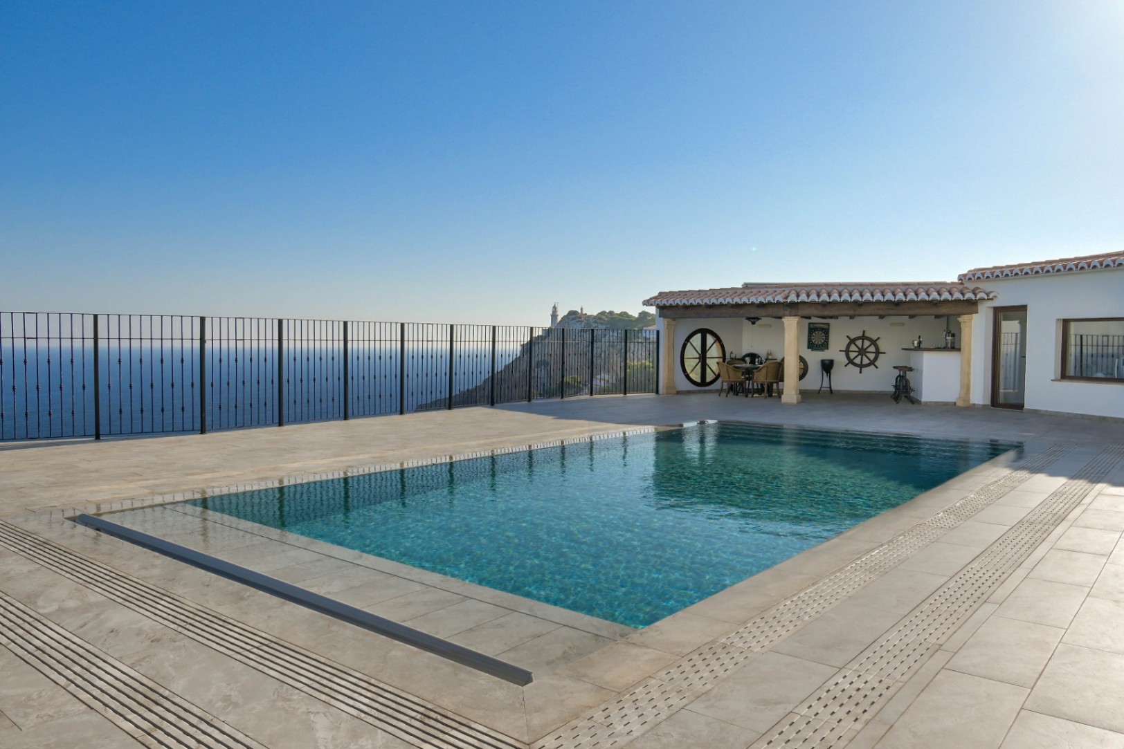 Piscine à débordement sur une terrasse en pierre avec vue panoramique sur la mer et le phare. Comprend un porche couvert avec coin repas et décoration nautique.