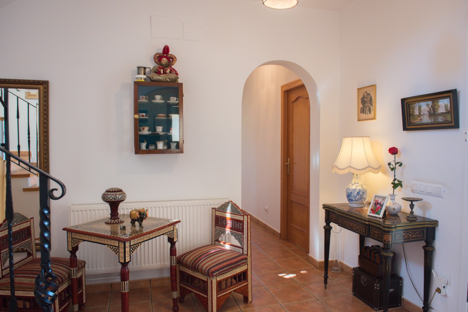 Hall d'entrée avec sol en terre cuite, passage voûté et mobilier en bois incrusté complété par une console décorative et une vitrine.