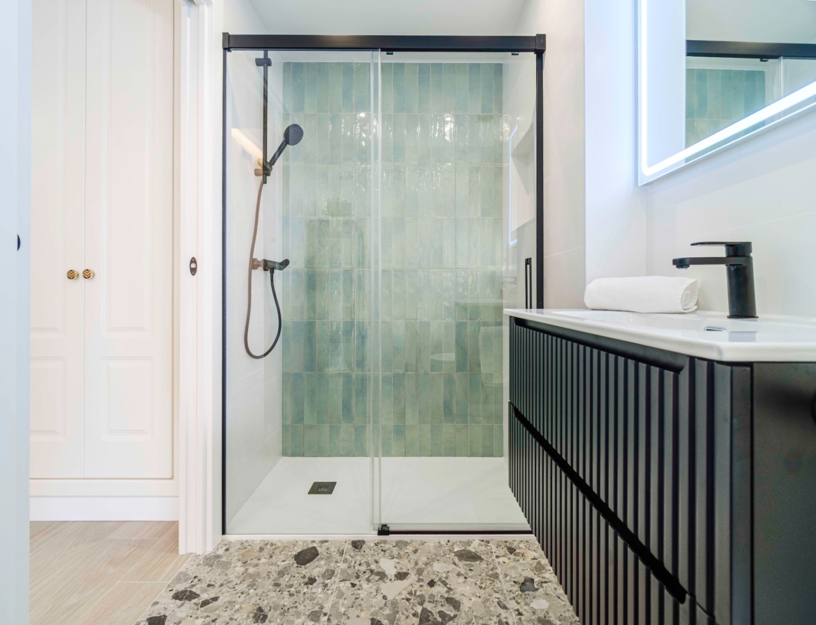Salle de bain moderne avec douche à l'italienne en carrelage turquoise vertical, robinetterie noire et meuble vasque à lattes avec miroir rétroéclairé.
