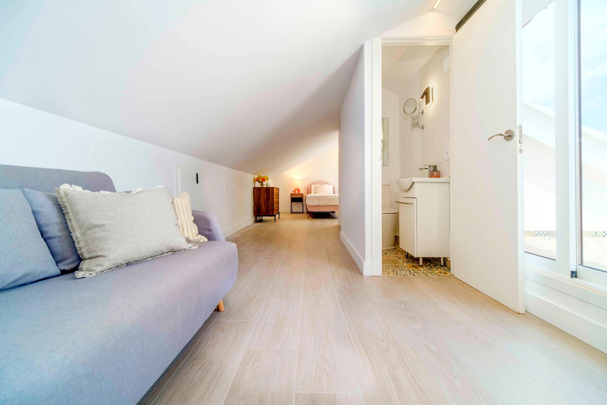 Suite mansardée lumineuse avec plafonds inclinés, sol en grès cérame aspect bois, espace salon et salle de bain attenante avec carrelage à motifs.