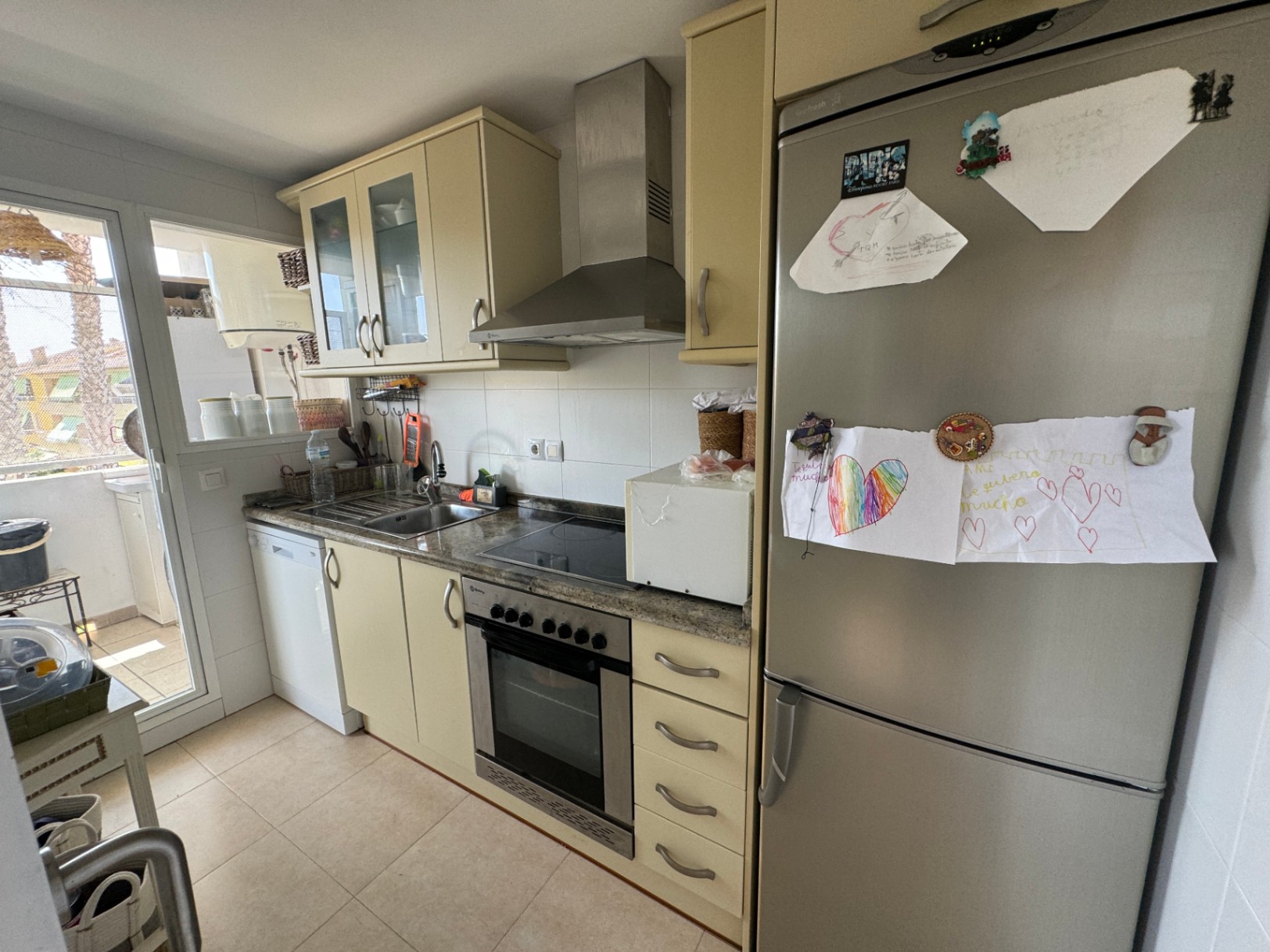 Cuisine fonctionnelle avec placards crème, plan de travail en granit et électroménagers en inox. Comprend un four encastré, une hotte et un accès direct à la terrasse.