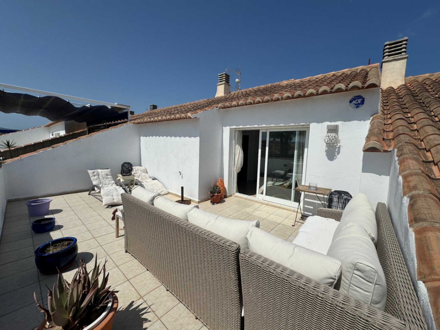 Terrasse privée avec salon en rotin, revêtement de sol en grès et accès par porte vitrée coulissante sous une toiture en tuiles canal.