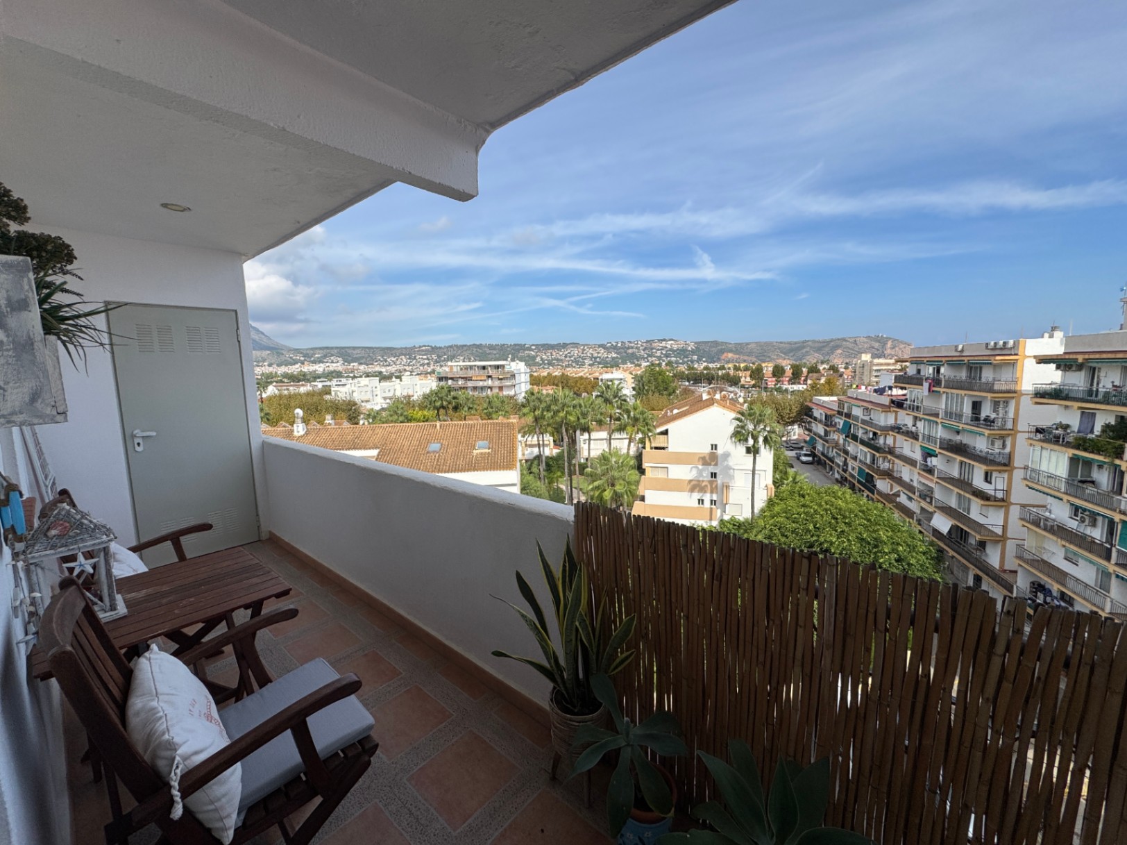 Balcon avec sol en terre cuite, mobilier en bois et brise-vue en bambou. Il offre une vue dégagée sur le paysage urbain et les montagnes environnantes.