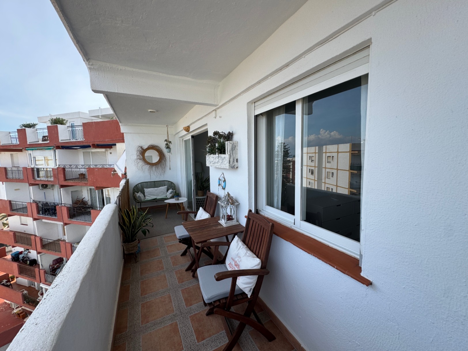 Balcon privé avec carrelage en terre cuite, ensemble de repas en bois et coin salon agrémenté d'un canapé en osier et d'un miroir décoratif.