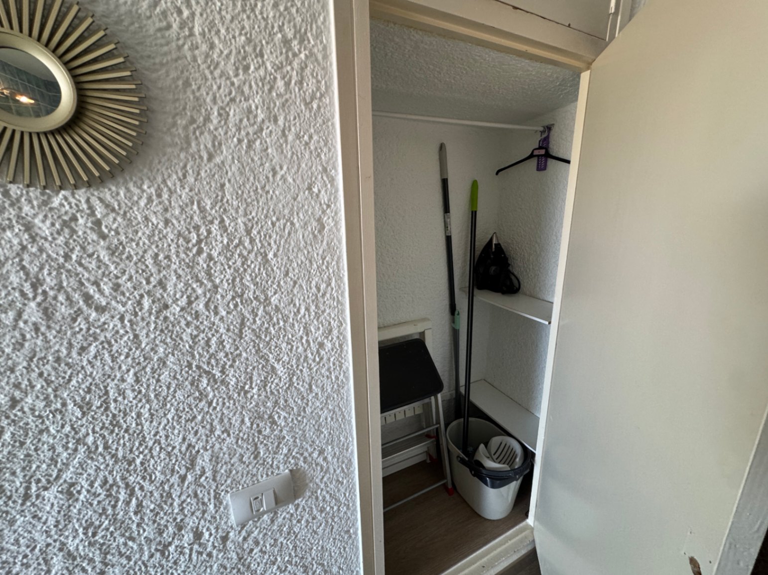 Petit placard de rangement utilitaire avec étagères blanches, tringle de penderie et espace pour le matériel d'entretien.