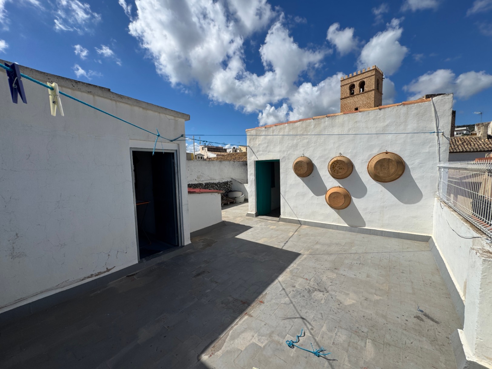 Terrasse de toit avec sol en dalles de pierre, murs blanchis à la chaux ornés de plats en terre cuite et vue sur un clocher historique.