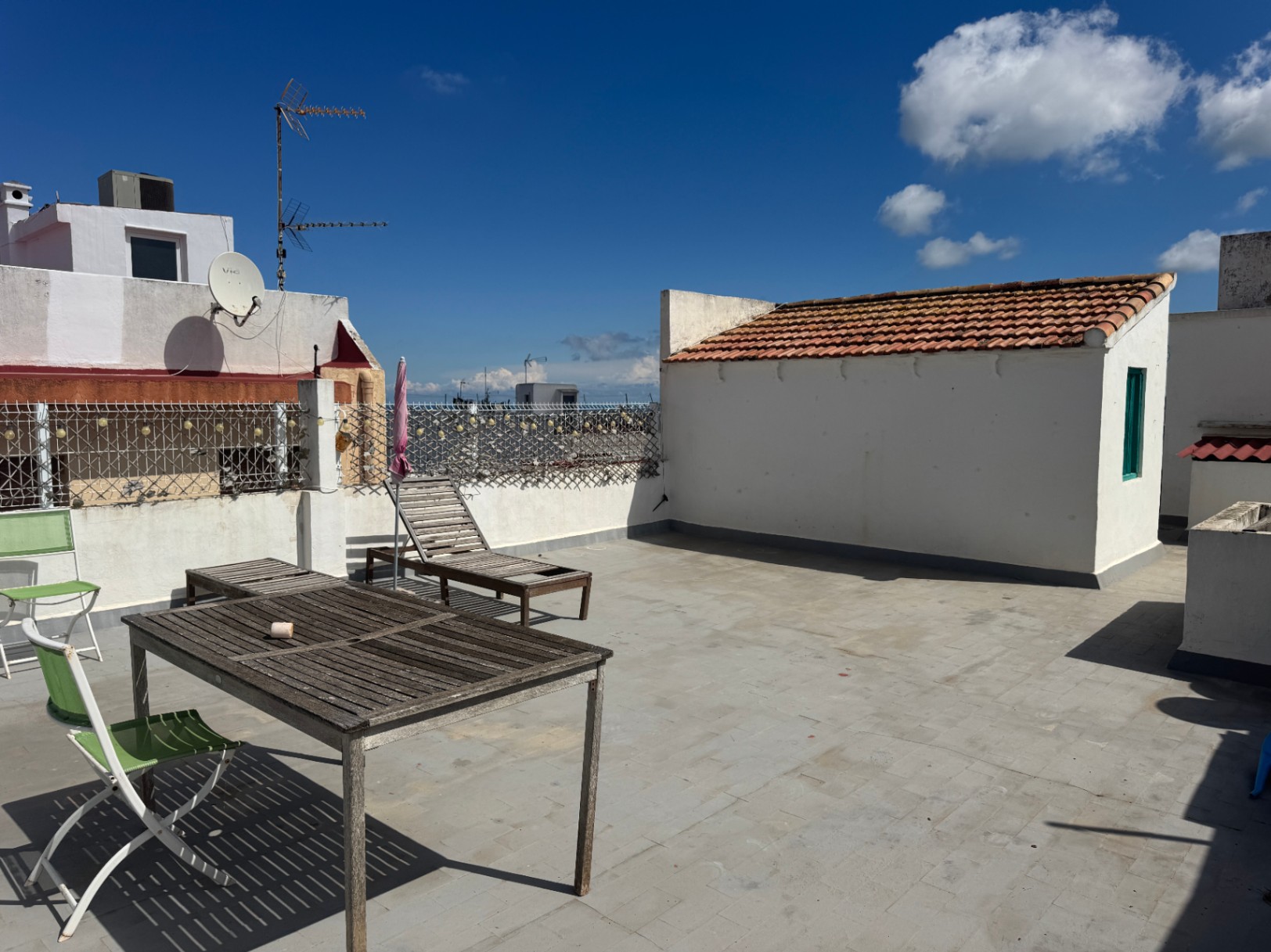 Vaste terrasse de toit avec sol en dalles grises, mobilier en bois patiné et murs blancs, offrant un espace extérieur dégagé.