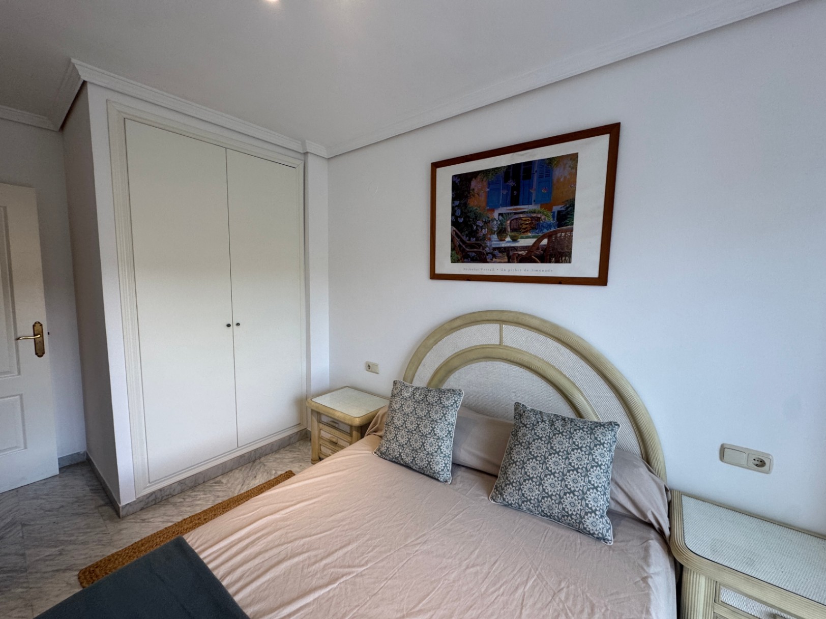 Chambre avec armoire encastrée blanche, sol en marbre et lit à tête de lit incurvée encadré par des tables de chevet assorties.