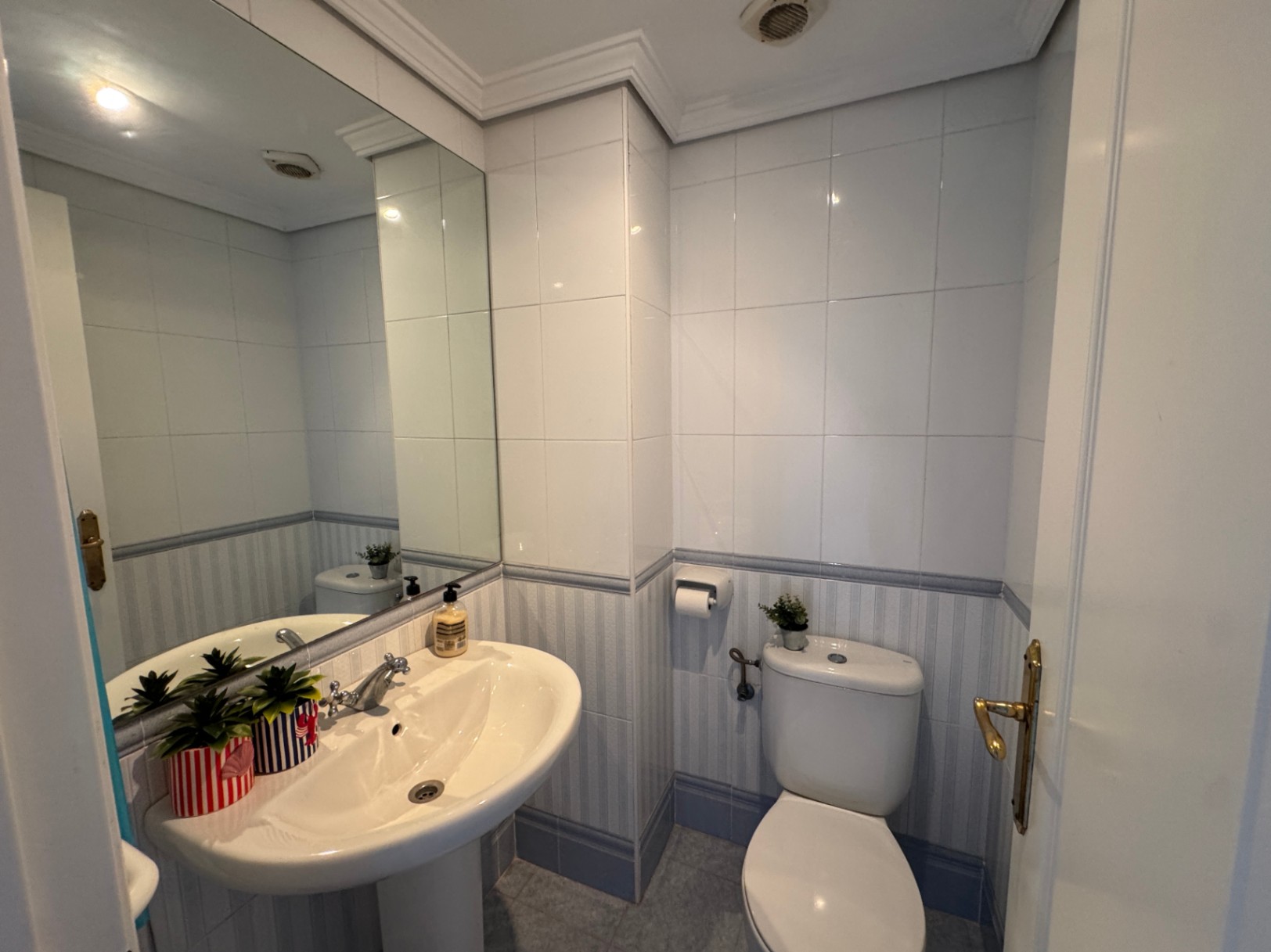 Salle de bain fonctionnelle avec lavabo sur colonne, grand miroir et murs carrelés agrémentés d'une frise décorative bleue.