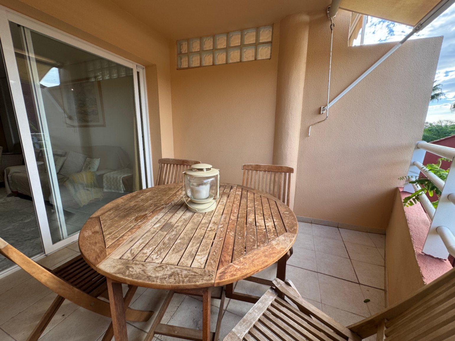 Terrasse couverte avec ensemble de repas en bois et sol carrelé, accessible par de grandes baies vitrées coulissantes depuis le salon.