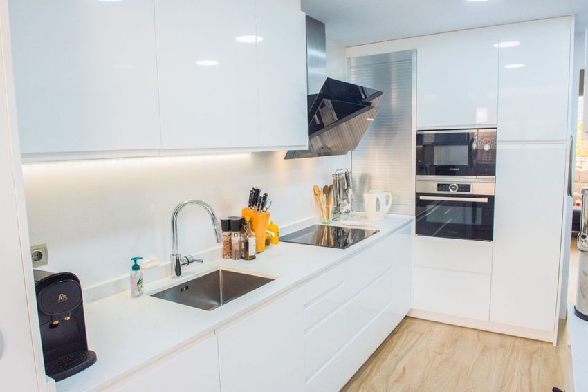 Cuisine moderne équipée d'armoires blanches laquées, d'appareils Bosch intégrés et d'un plan de travail blanc épuré. L'éclairage LED sous les meubles met en valeur l'évier et la plaque à induction. Cuisine moderne équipée d'armoires blanches laquées, d'appareils Bosch intégrés et d'un plan de travail blanc épuré. L'éclairage LED sous les meubles met en valeur l'évier et la plaque à induction.