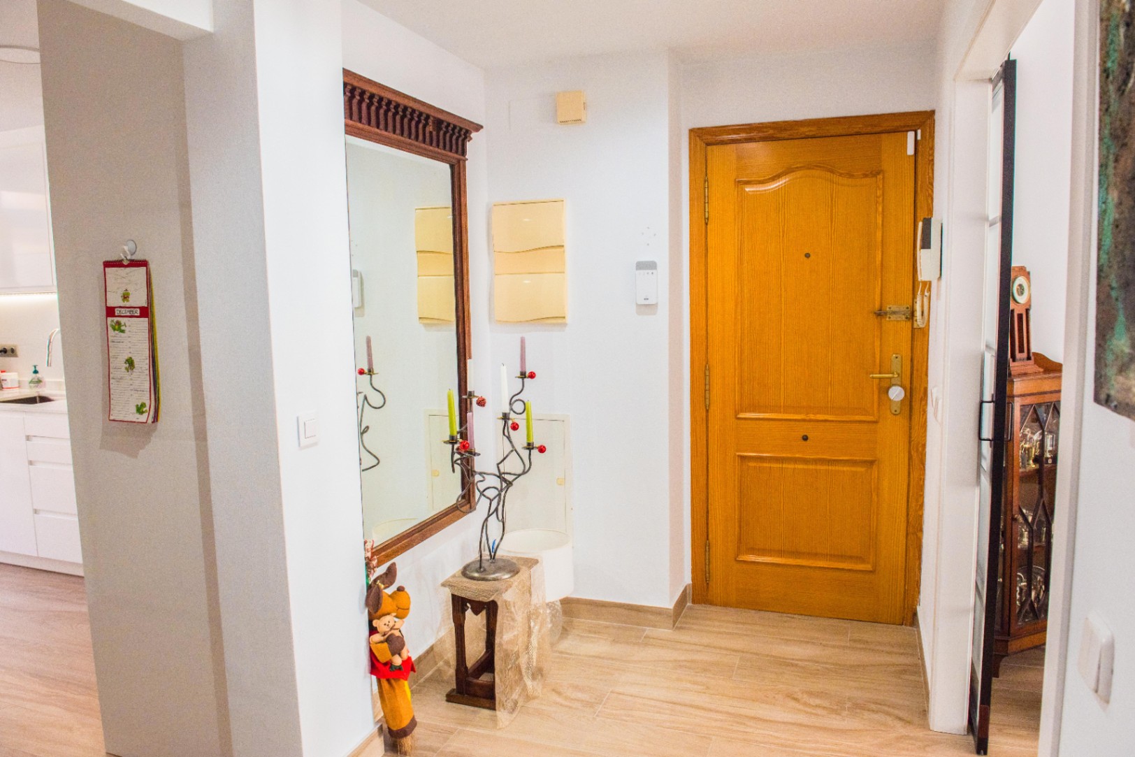 Entrée avec porte en bois massif, carrelage clair et grand miroir au cadre en bois sculpté. L'espace offre un accès direct à une cuisine moderne et lumineuse.