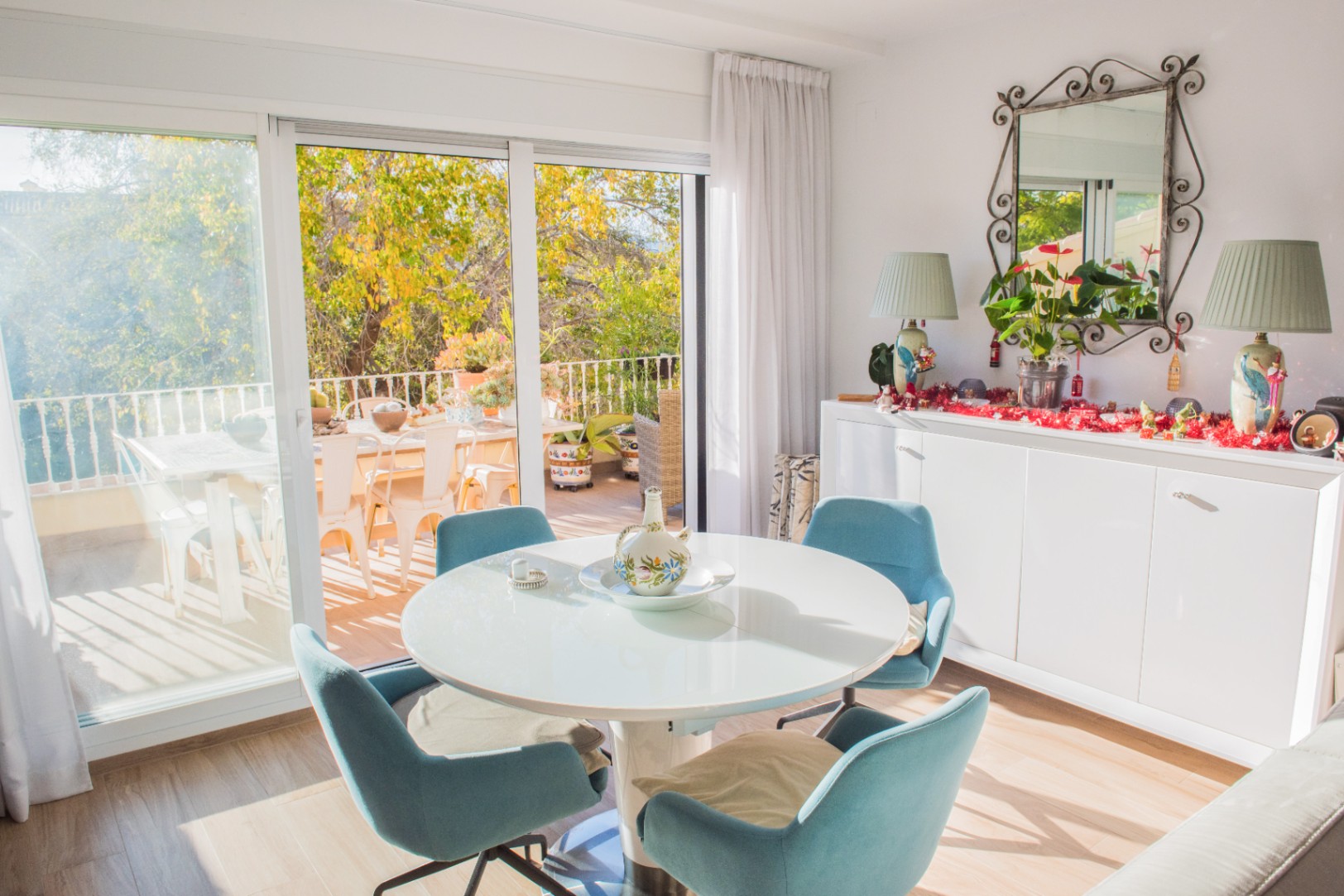 Salle à manger lumineuse avec table ronde blanche et chaises bleues, offrant un accès direct à une terrasse par de grandes baies vitrées.
