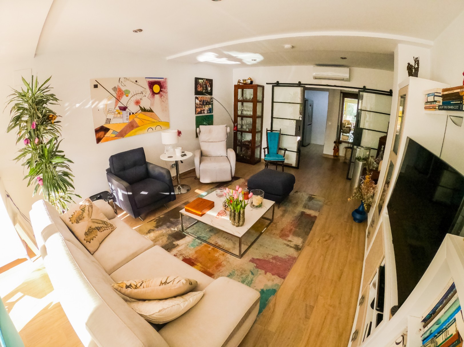 Salon contemporain avec canapé d'angle blanc, art abstrait et table basse en marbre sur tapis coloré. Des portes coulissantes de style industriel mènent aux pièces attenantes.