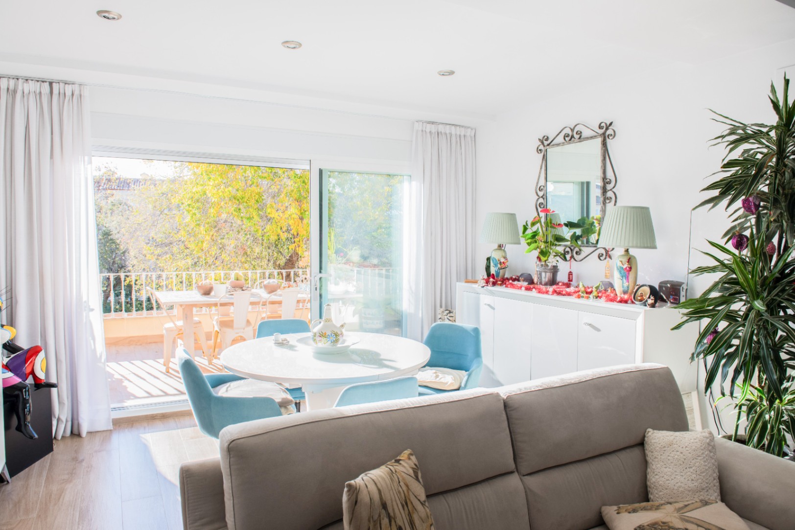 Salon lumineux comprenant un coin repas avec table ronde et chaises bleues, ouvert sur une terrasse aménagée offrant une vue sur la végétation.