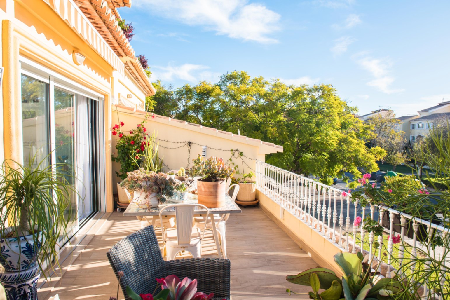 Terrasse avec carrelage imitation bois, espace dînatoire extérieur et balustrade blanche. Agrémentée de plantes en pots avec vue sur une végétation luxuriante.