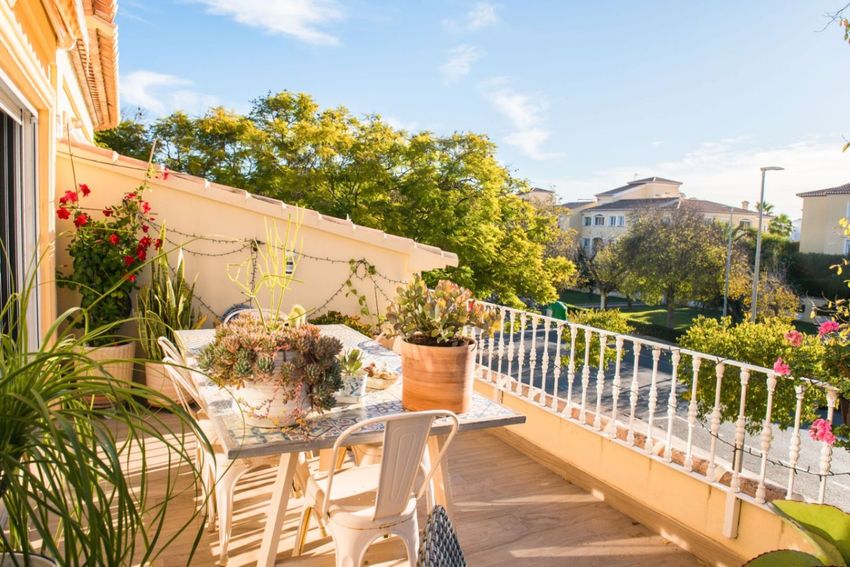 Terrasse ensoleillée aménagée avec une table mosaïque, des chaises en métal blanc et diverses plantes en pot. Des guirlandes lumineuses complètent la vue résidentielle. Terrasse ensoleillée aménagée avec une table mosaïque, des chaises en métal blanc et diverses plantes en pot. Des guirlandes lumineuses complètent la vue résidentielle.