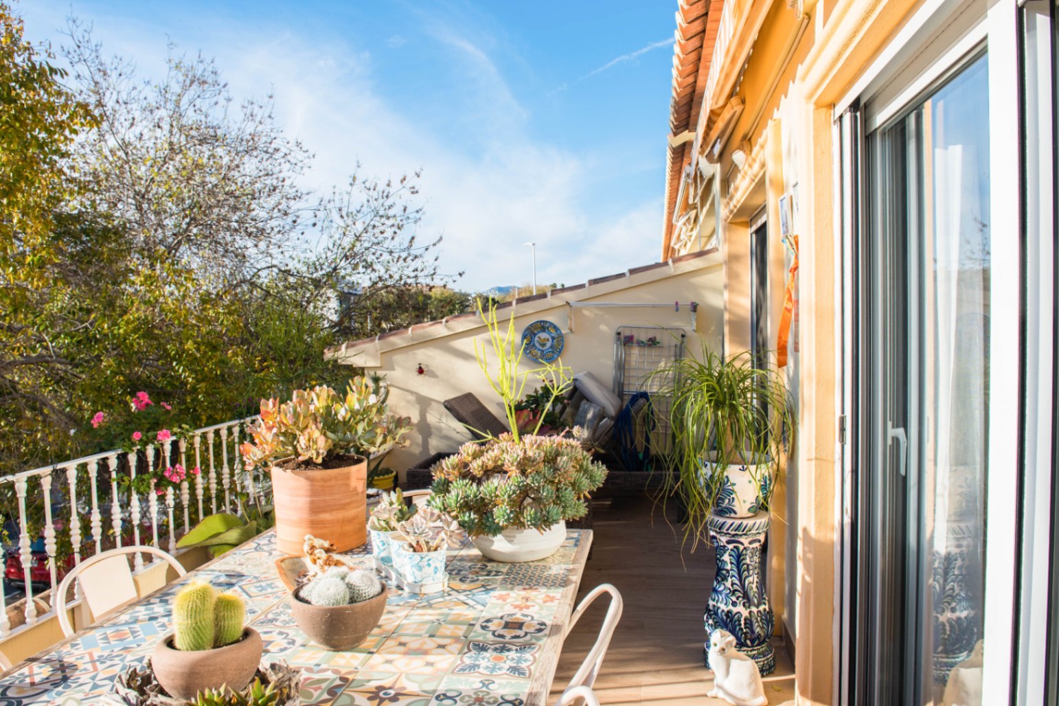 Terrasse extérieure avec table en carrelage ornemental, collection de succulentes en pots et accès par de larges baies vitrées coulissantes.