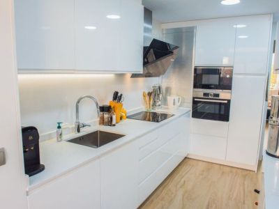 Cuisine moderne avec armoires blanches laquées, plan de travail clair et four et micro-ondes Bosch intégrés. Comprend une plaque à induction, un évier en inox et un éclairage sous les meubles.