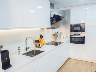 Cuisine moderne équipée d'armoires blanches laquées, d'appareils Bosch intégrés et d'un plan de travail blanc épuré. L'éclairage LED sous les meubles met en valeur l'évier et la plaque à induction.