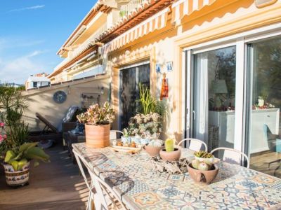 Grande terrasse ensoleillée dotée d'une table à manger en mosaïque, de diverses plantes succulentes en pot et de sièges confortables. Des auvents rayés offrent de l'ombre et un accès direct à l'intérieur.