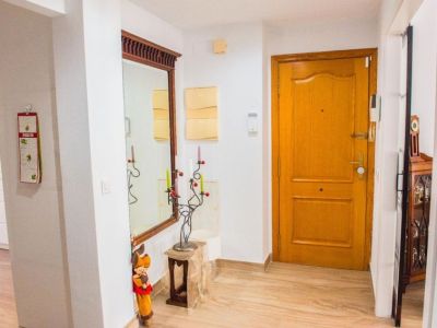 Le hall d'entrée accueillant dispose d'une porte d'entrée en bois clair, d'un carrelage effet bois et d'un grand miroir encadré. Une partie de la cuisine moderne est visible à gauche.