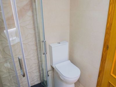 Salle de bain moderne présentant des toilettes blanches et une cabine de douche vitrée avec poignées chromées. Le carrelage mural beige est texturé de motifs de feuilles dans la douche.