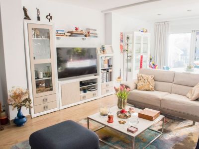 Salon lumineux avec canapé beige confortable, table basse moderne en marbre et meuble TV blanc. La lumière naturelle inonde l'espace via de grandes portes vitrées.