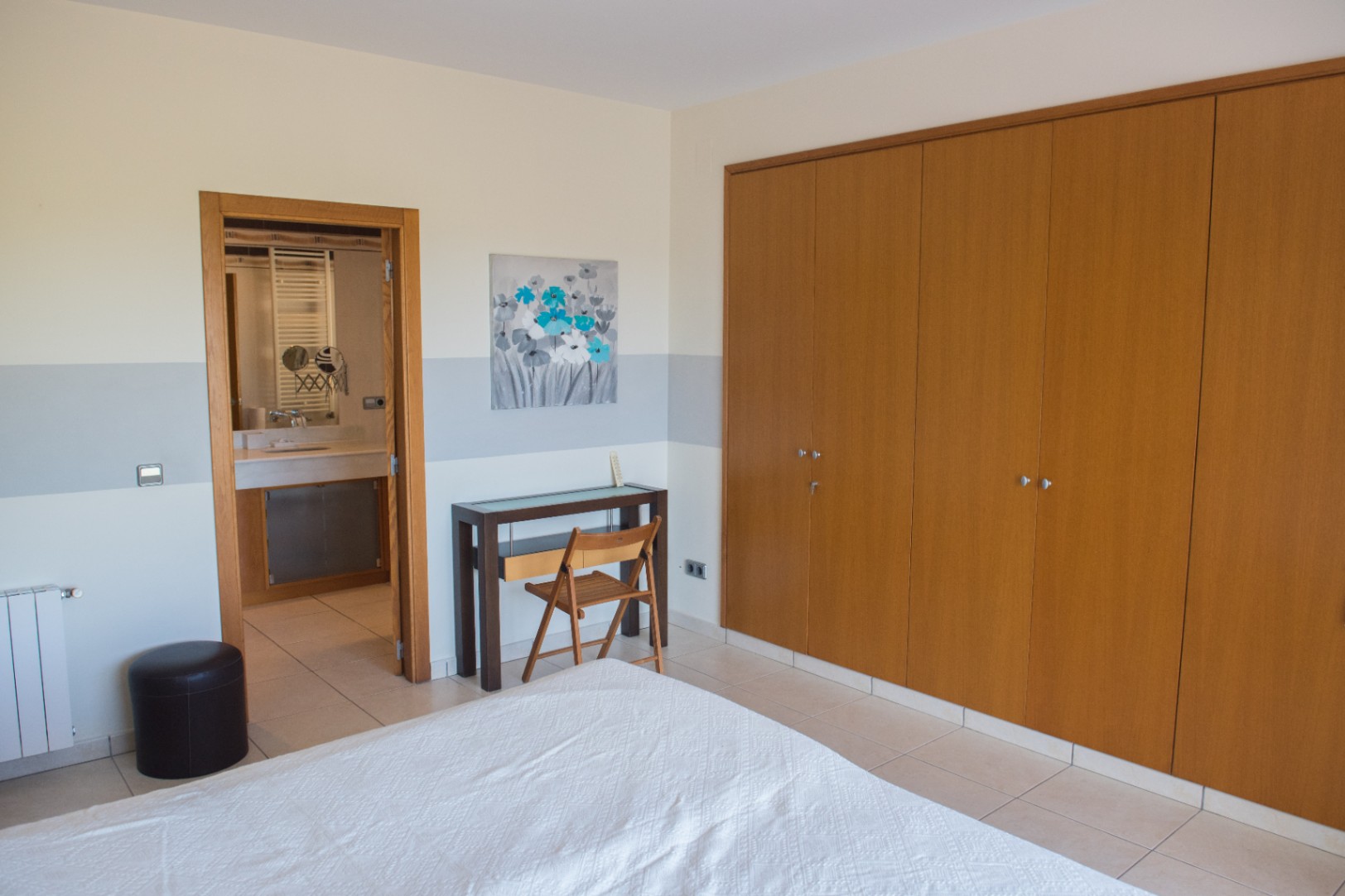 Chambre avec grand placard intégré en bois, espace bureau et vue sur la salle de bain attenante avec sol en carrelage.