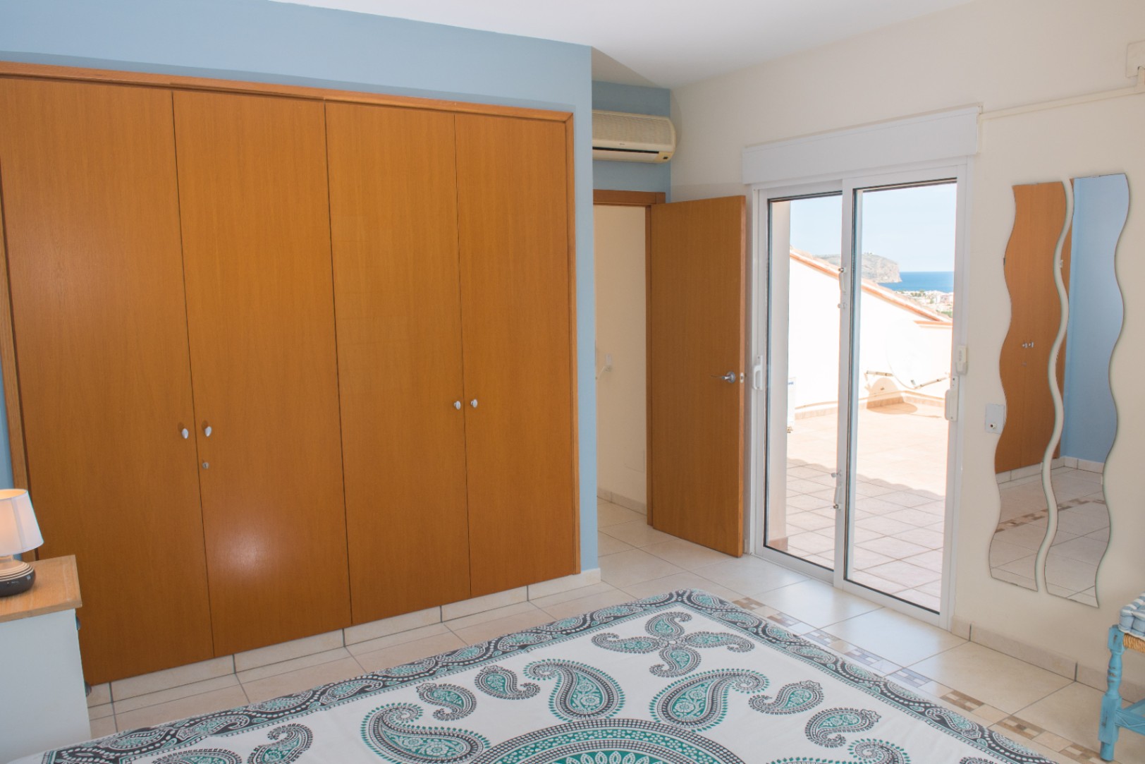 Chambre avec grand placard intégré en bois, murs bleu ciel et accès direct à une terrasse privée offrant une vue sur la mer Méditerranée.