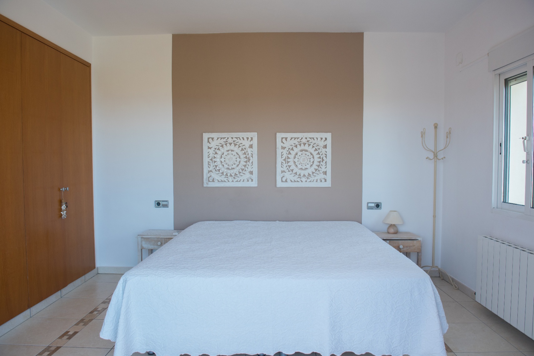 Chambre avec mur d'accent taupe, panneaux décoratifs sculptés, armoire en bois intégrée et sol en carrelage avec bordure ornementale.