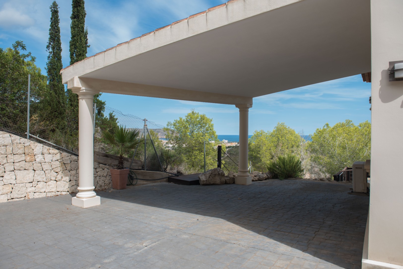 Espace de stationnement couvert avec colonnes de style classique, pavés gris et vue panoramique sur le littoral méditerranéen et les cyprès.