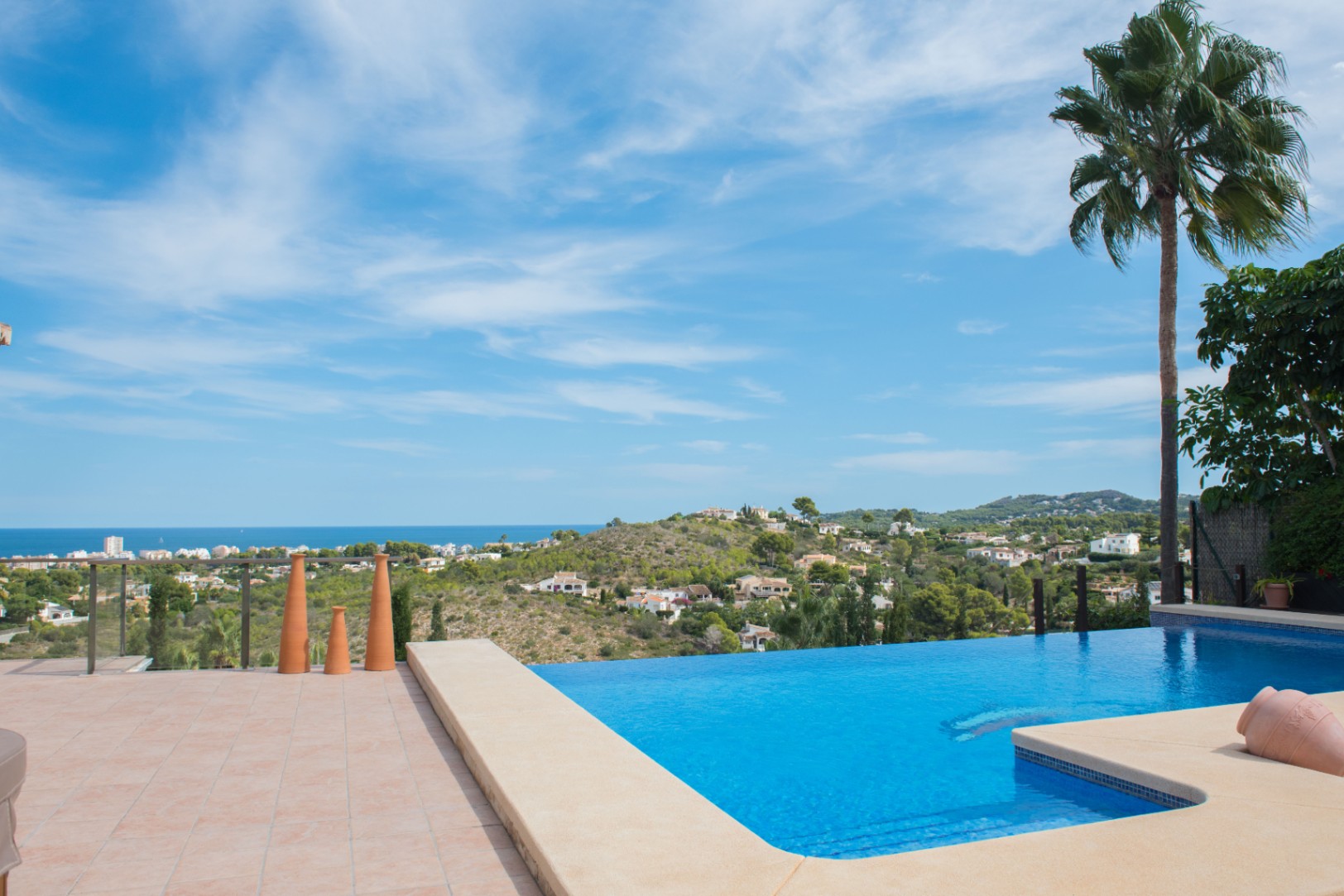 Piscine à débordement avec margelle en pierre et vue panoramique sur la mer. La terrasse est revêtue de terre cuite et d'éléments décoratifs.