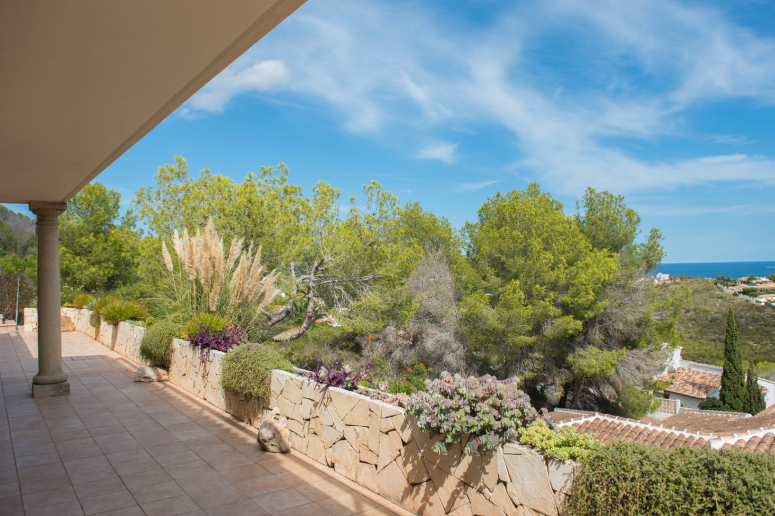 Terrasse couverte avec carrelage en terre cuite et jardinière en pierre naturelle, offrant une vue sur la pinède et la mer à l'horizon.