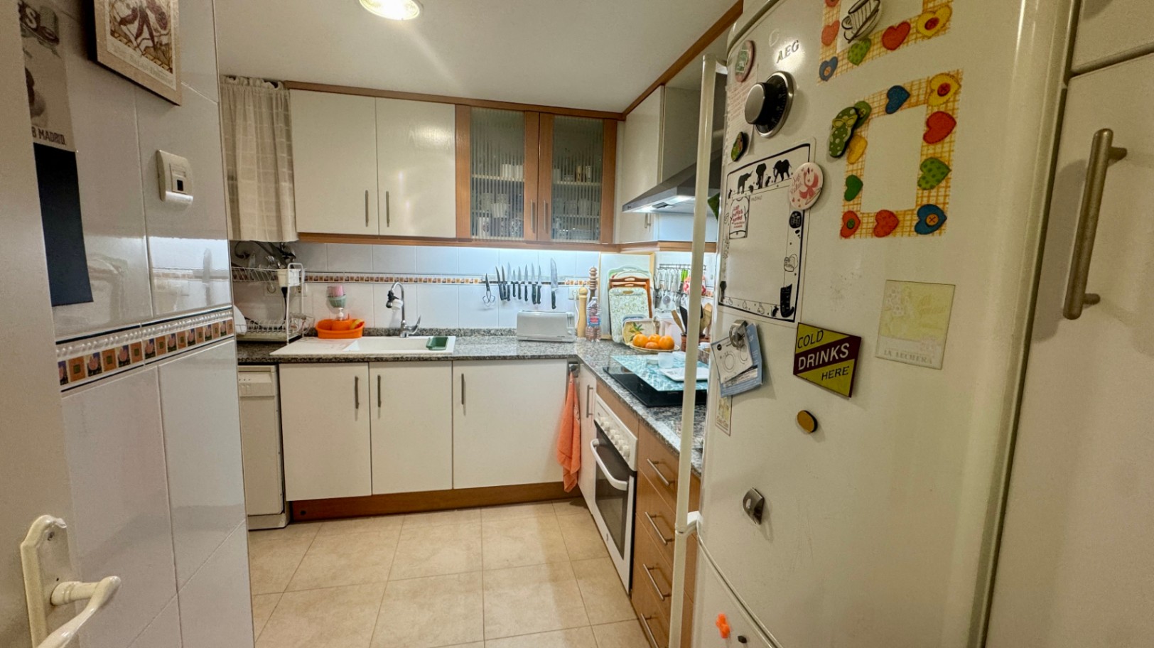 Cuisine fonctionnelle en L avec des placards blancs bordés de bois, un plan de travail en granit moucheté et un éclairage sous les meubles hauts.