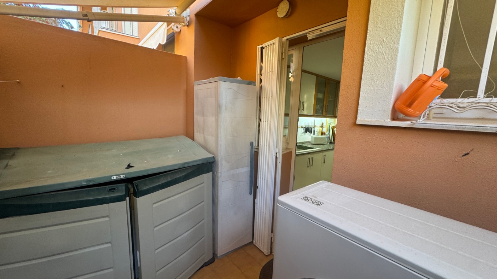 Patio de service aux murs ocre comprenant des unités de rangement extérieures et un accès direct à la cuisine par une porte pliante.