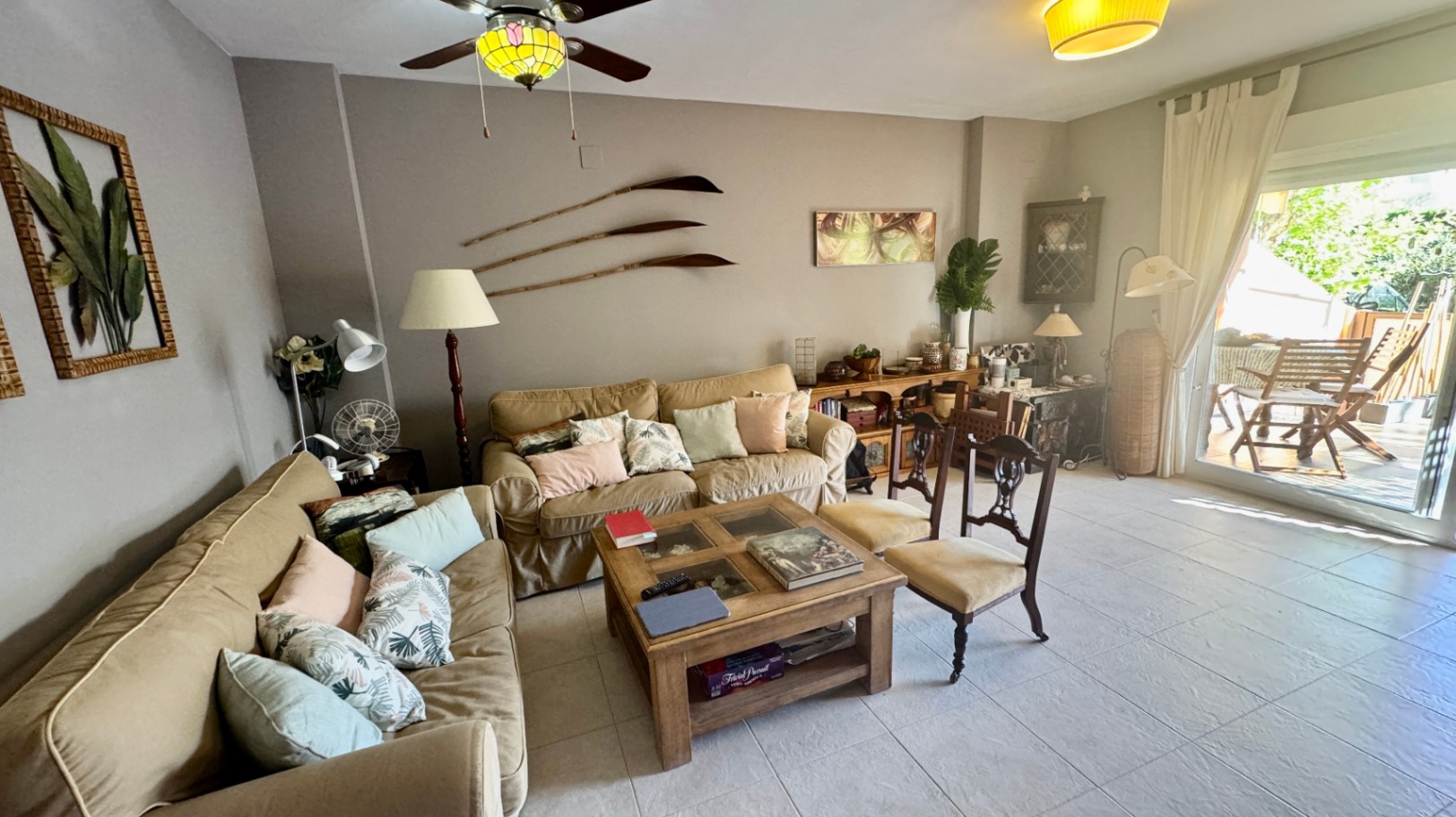 Salon équipé de canapés beiges, d'une table basse en bois massif et d'un accès vers une terrasse extérieure ensoleillée.