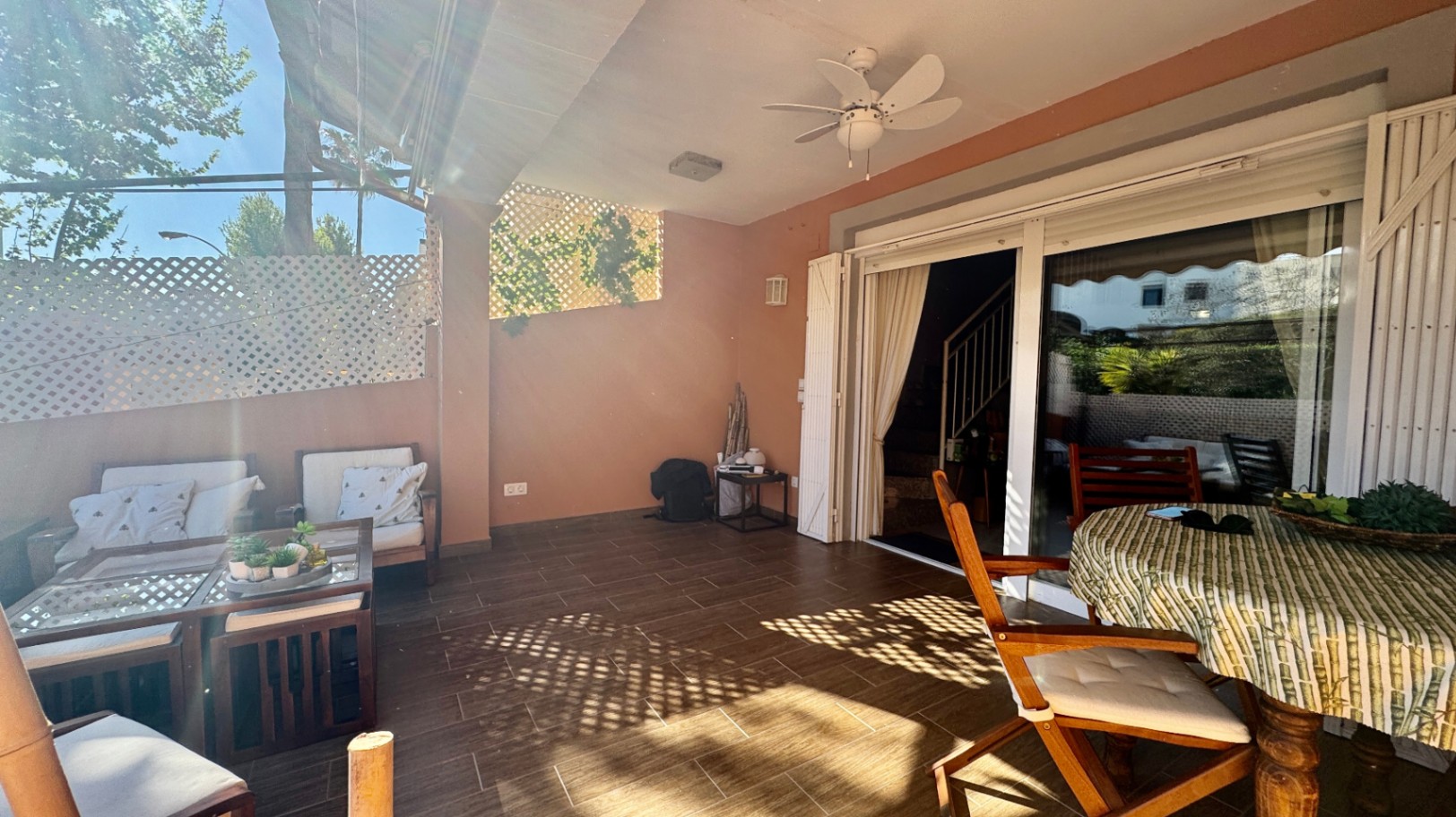 Terrasse couverte avec sol en grès cérame, ventilateur de plafond et baies vitrées coulissantes. Comprend un coin salon et un espace repas extérieur avec treillis.