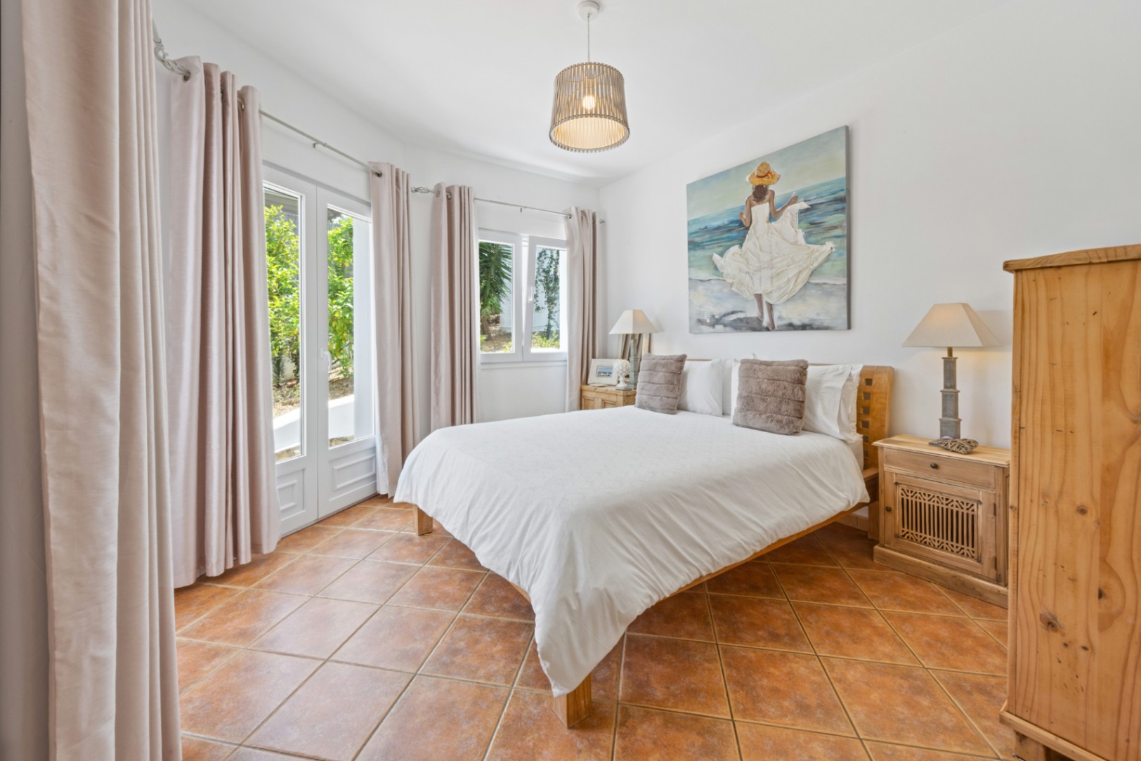 Chambre lumineuse avec sol en terre cuite, mobilier en bois et doubles portes vitrées offrant un accès direct au jardin et une belle clarté.