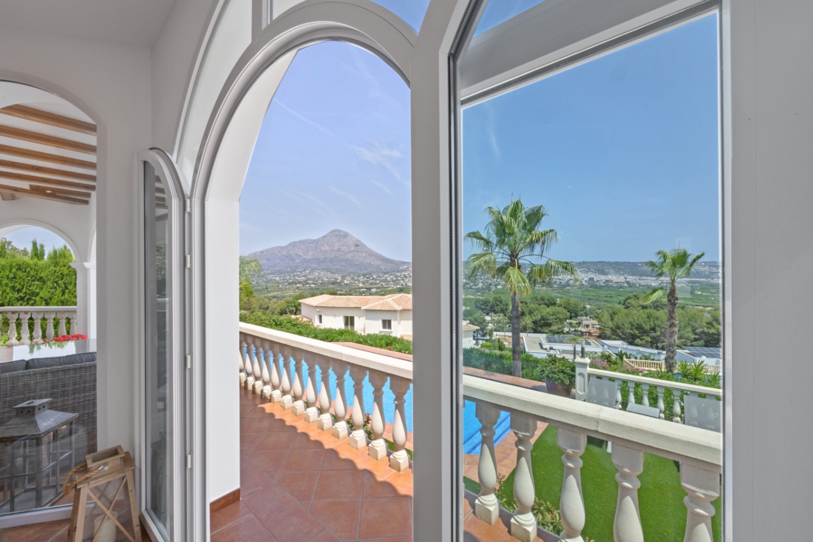 Des fenêtres cintrées blanches cadrent une vue panoramique sur la montagne et la vallée, surplombant une terrasse en terre cuite et sa piscine privée.